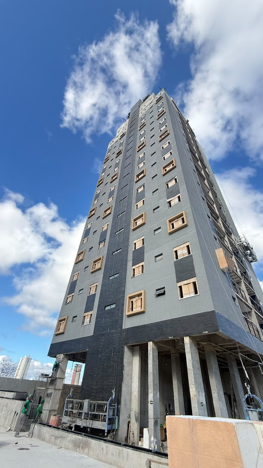 Fachada do Van Gogh Residencial vista do térreo, com revestimento cinza e preto já aplicado nos pavimentos altos e estrutura de concreto aparente na base